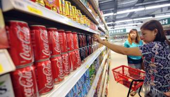 A woman takes a can of Coca-Cola from a shelf at a supermarket.
