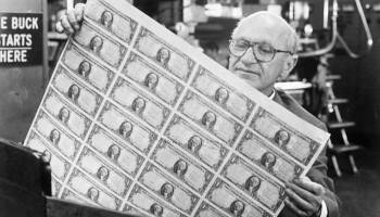 Milton Friedman holds a sheet of printed money.