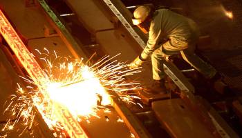 A steelworker in protective gear crouches next to a spark burst