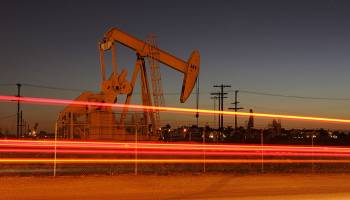 Car lights streak past an oil rig extracting petroleum in Culver City, California.