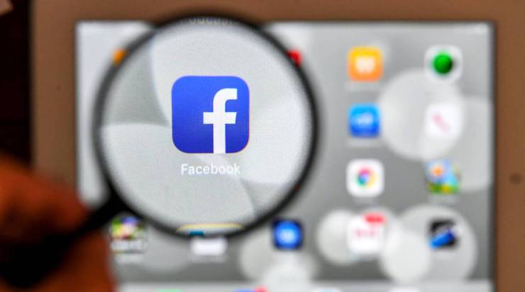 A tablet screen displays the logo of the social networking site Facebook through a magnifying glass.