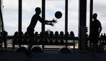 Silhouette image of a man throwing a weighted ball in a gym as another person observes.