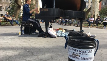 A piano player performs in Washington Square Park. His tip bucket also has his Venmo account information.