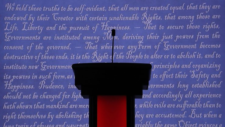 A red and black debate lectern with a slim microphone against a stage background featuring the words to the declaration of independence.
