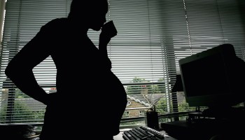 In this photo illustration a pregnant woman is seen standing at an office work station.