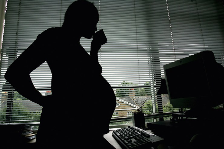 In this photo illustration a pregnant woman is seen standing at an office work station.