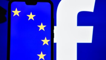 The European Union Flag is seen displayed on an Android mobile phone with Facebook logo in the background