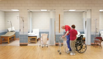 A physical therapy aide helps a man exercise at a nursing home.