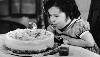 A little girl blows out candles on her birthday cake circa 1950. Adults seem to be increasingly nostalgic for their childhoods.