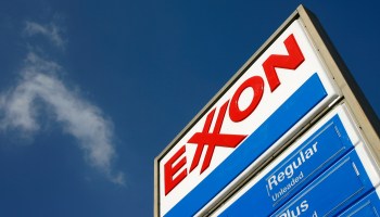 An Exxon gas station sign against a blue sky with a small cloud.