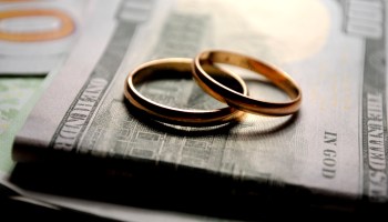 Two gold wedding bands sit on a $100 bill.