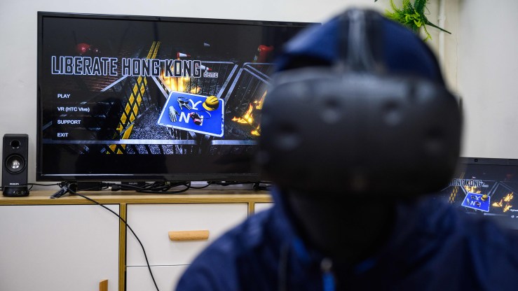 In this picture taken in Hong Kong on October 28, 2019, an unidentified member of the team who designed and programmed the Liberate Hong Kong computer game, based on the current protests taking place in the city, poses in a virtual reality control kit in front of a monitor showing the game at a warehouse space in the Kowloon district.