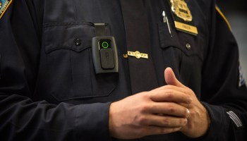 A closeup of a police officer in uniform with a body camera on his breast pocket.
