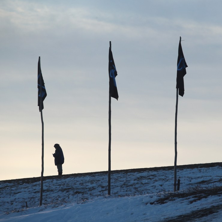 A woman appears to look at a phone under tribal flags at the Standing Rock Sioux Reservation in 2016.