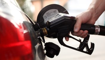 A hand holds a gas nozzle inserted in a car's tank.
