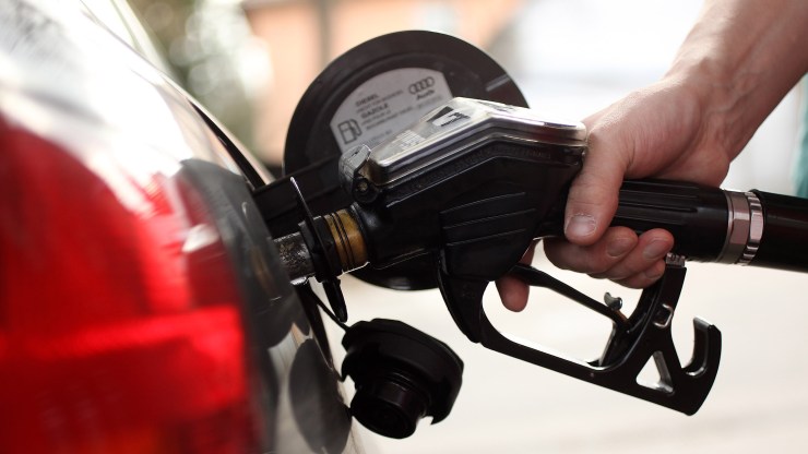 A hand holds a gas nozzle inserted in a car's tank.
