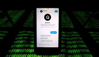 The Quartz chatbot is displayed on a cellphone above streams of binary code in this photo illustration.