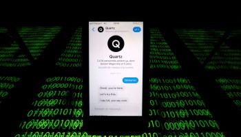 The Quartz chatbot is displayed on a cellphone above streams of binary code in this photo illustration.