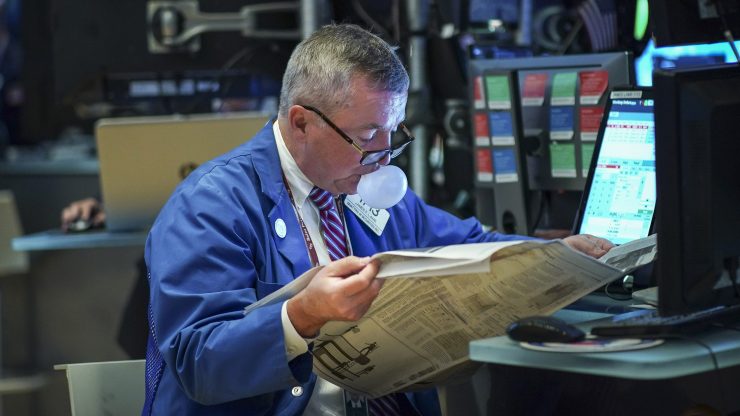 A trader reads the newspaper and blows a bubble on the floor of the New York Stock Exchange at the opening bell on Au. 19, 2019.
