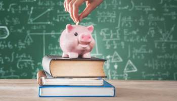 A piggy bank on top of textbooks in front of a chalkboard