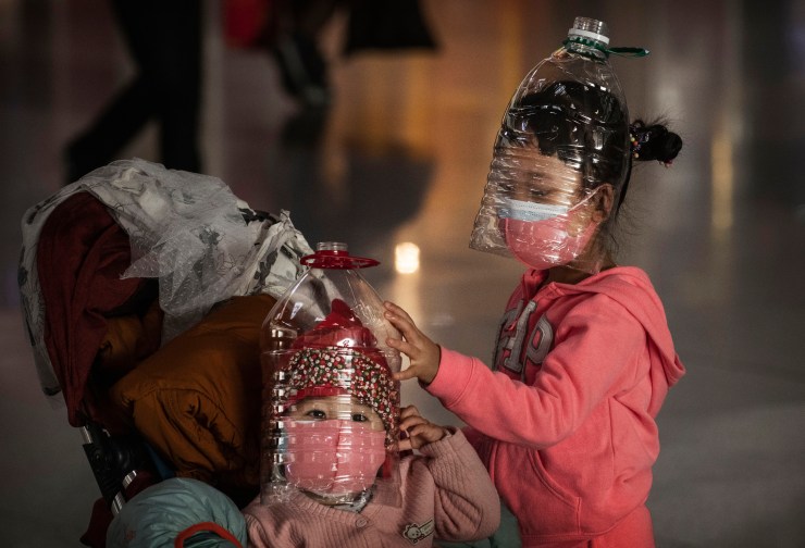 Chinese children wear plastic bottles as makeshift homemade protection and protective masks while waiting to check in to a flight at Beijing Capital Airport on January 30, 2020.