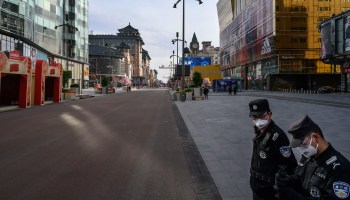 Chinese security guards wear protective masks as they guard a nearly empty commercial street Tuesday in Beijing.