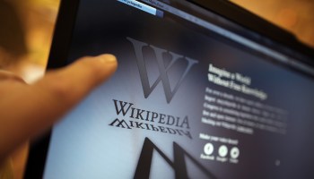 A laptop computer displays Wikipedia's front page showing a darkened logo.