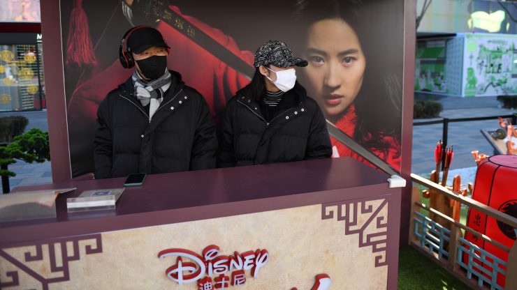 Two people wearing face masks work a promotional stand for the Disney movie "Mulan" in an almost empty shopping mall in Beijing.