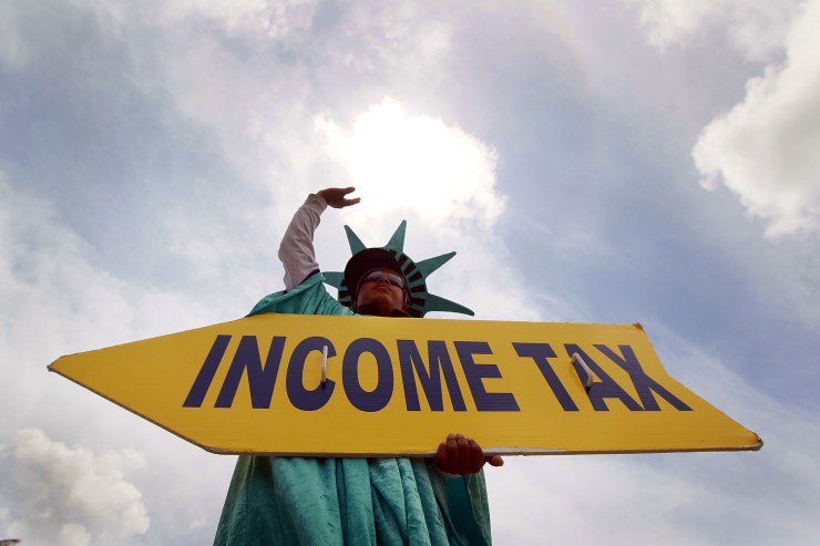 A person dressed as the Statue of Liberty holds a sign reading "Income Tax."