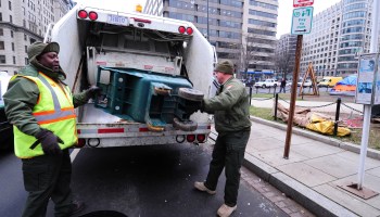 Two sanitation workers put trash into a garbage truck.