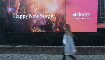 A woman walks past an ad for Tinder