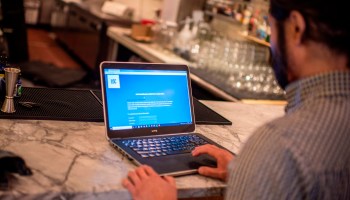 A person sits at a laptop at the marble counter of a bar.