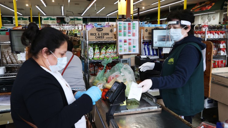 A cashier wears mask, gloves and a plastic visor at the checkout station Pat's Farms grocery store on March 31 in Merrick, New York