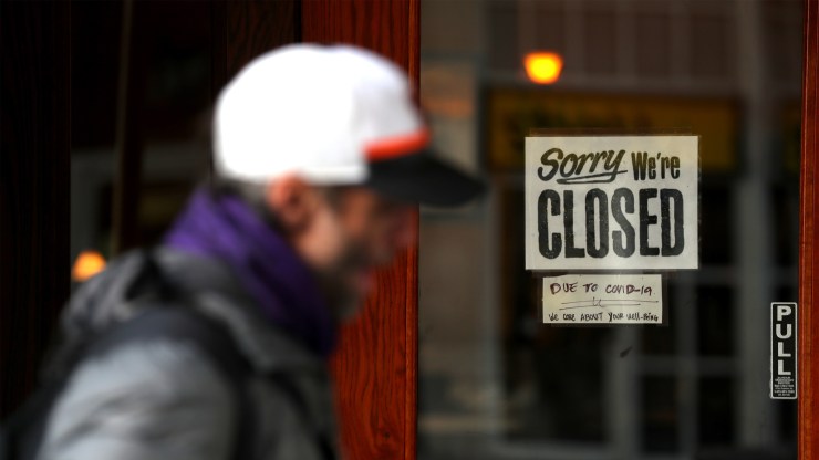 A pedestrian passes a "closed" sign on a restaurant in San Francisco.