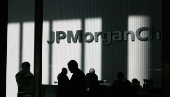 The words "JPMorgan Chase" appear inside an office, with dramatic shadows creating dark, vertical stripes on the well. People in the office, heads bent, appear in silhouette.