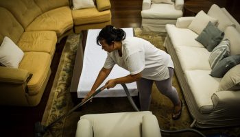 A housekeeper vacuums around couches.