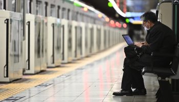 A man works on his laptop while waiting for a train in Tokyo in April.