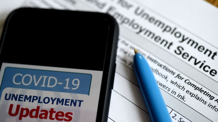 A COVID-19 Unemployment Assistance Updates logo is displayed on a smartphone on top of an application for unemployment benefits.