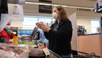 A woman wearing a mask at a grocery store checkout stand.