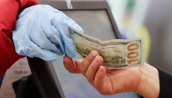 A woman pays cash while wearing gloves at a grocery store.