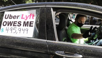 A driver's sign says Uber and Lyft owe him money.