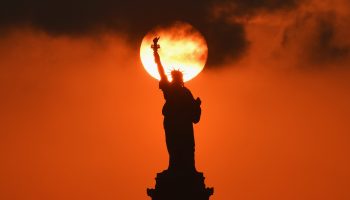 The sun sets behind the Statue of Liberty, an iconic symbol of welcome.