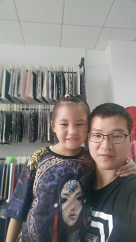 Zhang Baoguo (right) and his daughter pose in front of samples of fabric, which are usually destined for overseas markets like the U.S. but all of his overseas clients cancelled their orders because of the pandemic. (Courtesy of Zhang Baoguo)