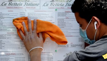 An employee cleans the posted menu of a reopened Virginia restaurant. Menus have downsized as the industry's revenue declined.