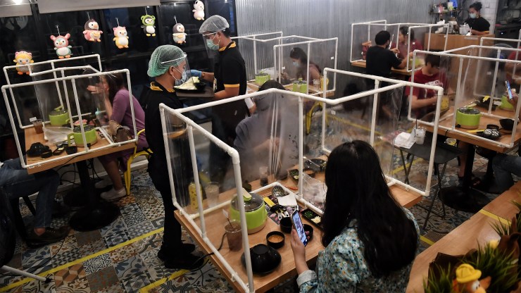 People at a Bangkok restaurant eat within plastic partitions set up to contain the potential spread of the coronavirus. Some businesses are adding charges for such equipment.