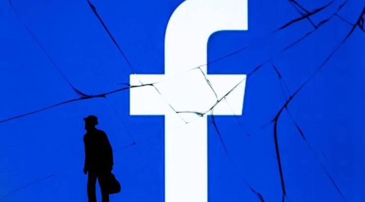 This photograph taken on May 16, 2018, shows a figure standing in front of the logo of social network Facebook on a cracked screen of a smartphone in Paris.