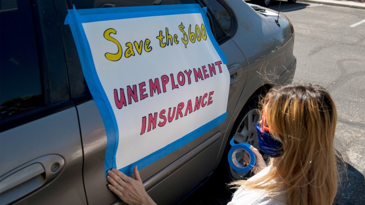 An activist in Las Vegas tapes a sign to her car in support of extending the $600 weekly unemployment benefit, which expired at the end of July.