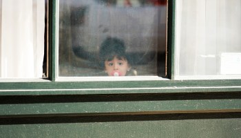 A child with a pacifier looks out a window in New York City.