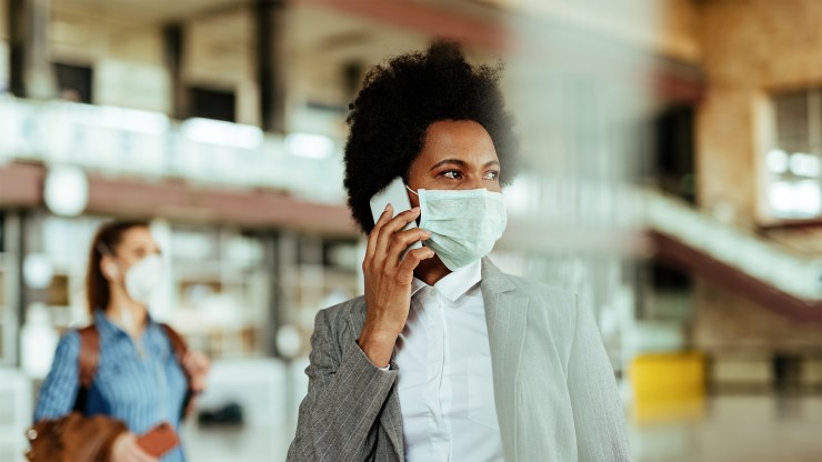 A Black businesswoman wearing a face mask speaks on a cellphone.