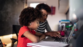 A mother helps her home-schooled daughter learn on a laptop. Parents are buying furniture and equipment to help their kids continue their education at home.